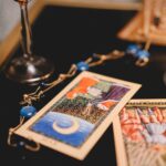 Vários baralhos ciganos coloridos abertos sobre uma mesa de madeira rústica, mostrando cartas e manuais de guia detalhados.