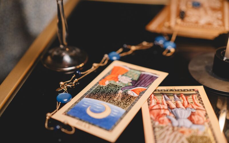 Vários baralhos ciganos coloridos abertos sobre uma mesa de madeira rústica, mostrando cartas e manuais de guia detalhados.