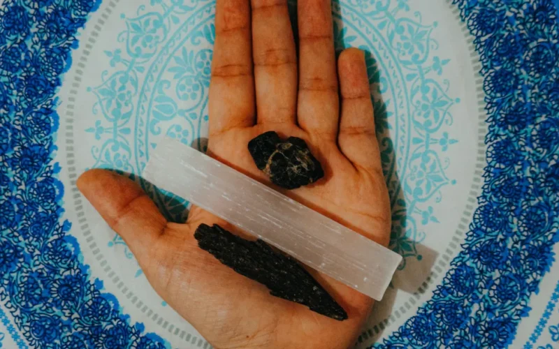 Turmalina Negra bruta sobre uma placa ou bastão de Selenita branca em um ambiente de luz suave.