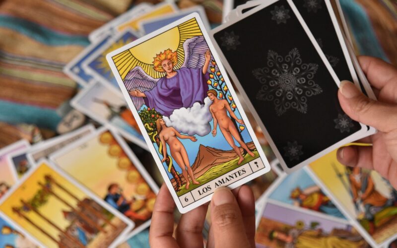 Três baralhos de tarot abertos sobre uma mesa de madeira rústica com velas e cristais de quartzo rosa